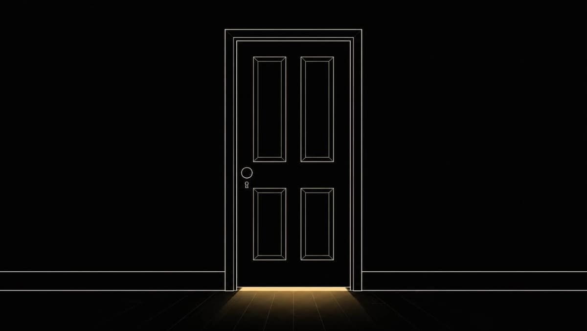 A closed door in a dark room, with warm light glowing through the gap beneath it.