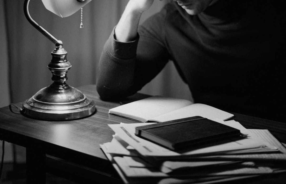 A writing desk at night: a lamp, an open notebook, and a stack of letters.
